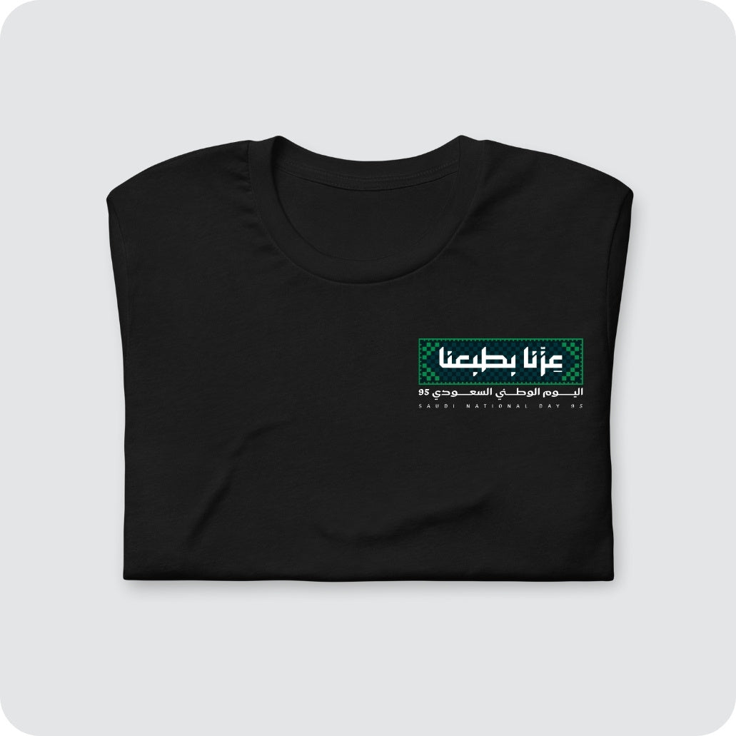 تيشيرت اليوم الوطني السعودي عزنا بطبعنا بخلفية سوداء بتصميم تراثي أخضر